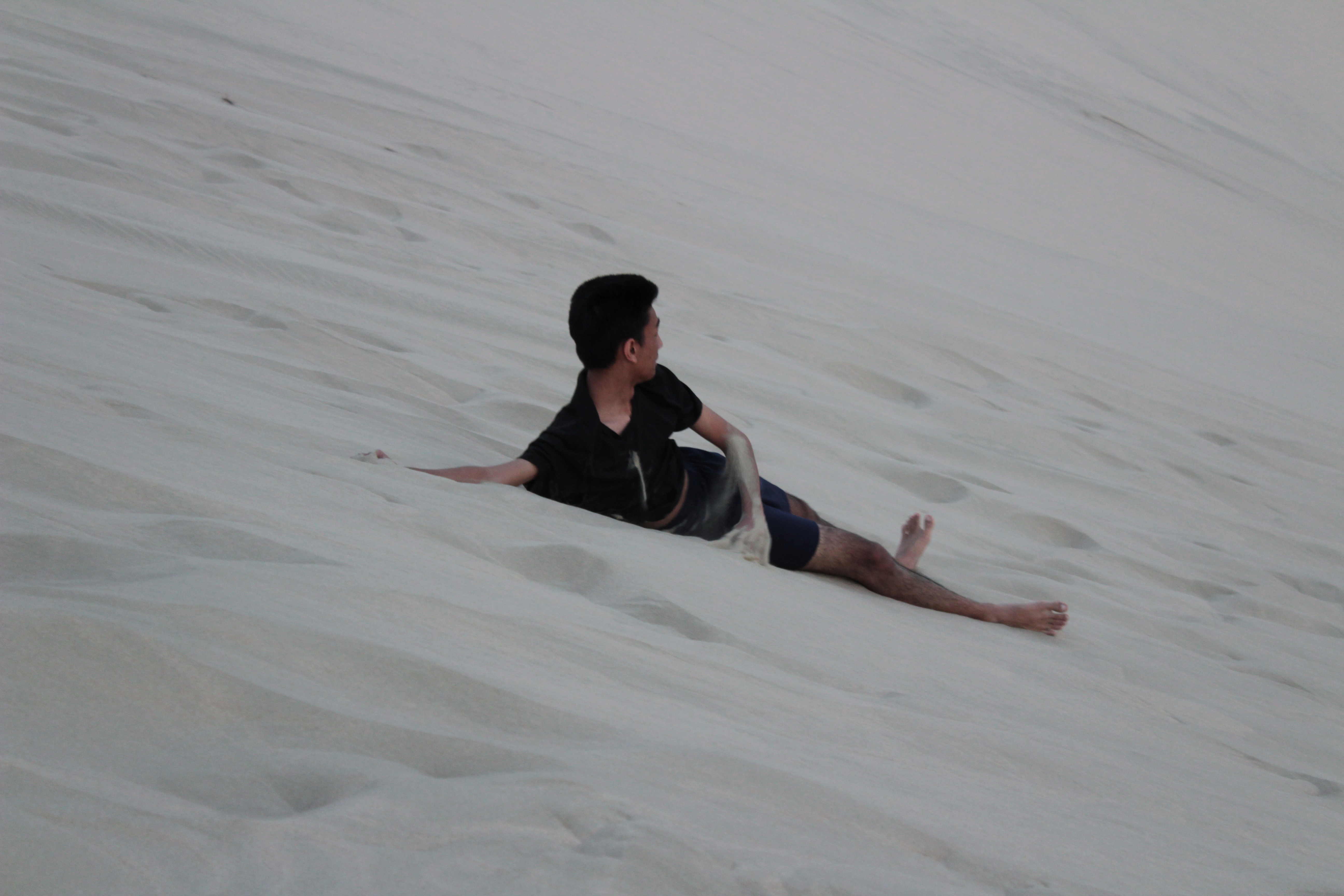 student sliding down sand dune
